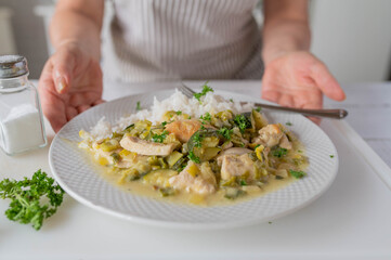 Woman serving a healthy meal with chicken breast in a delicious leek sauce and rice on a plate in the kitchen.