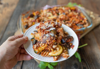 Plate with delicious vegetarian pasta casserole. Cooked with ratatouille vegetables such as zucchini, tomatoes and eggplant. Topped with parmesan cheese and pine nuts