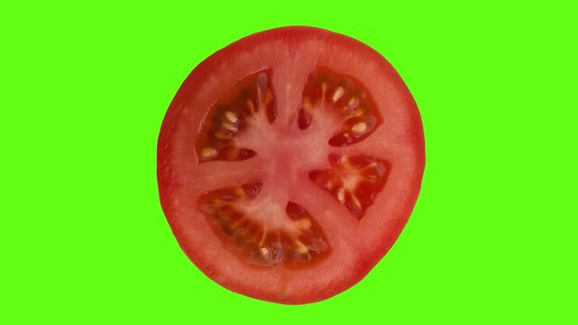 Slice of fresh tomato rotating on the green screen. Macro detail of cut tomato slice with seeds spinning on the chroma key background. 
