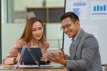 Two employees in a modern office, an Asian man and a woman working at a table, colleagues discussing and consulting, thinking about a joint project.