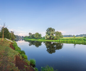 A serene river weaves through a green landscape, mirroring the sky and trees. Morning light bathes everything in a warm, peaceful glow