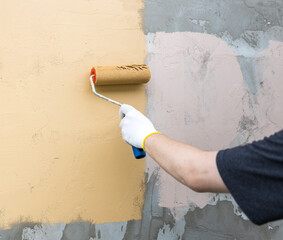 A person is painting a wall with a roller, using a yellow and white color