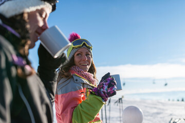 Friends enjoying a sunny winter day on the mountain, sipping tea and basking in the snowy...