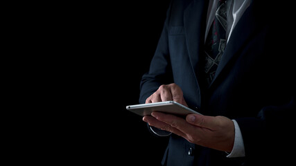Close-up of a businessman in a suit interacting with a tablet against a dark background, focusing on modern technology and professionalism
