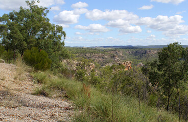 View of rocky outcrops, trees, grass and blue sky at Isla Gorge in Queensland, Australia