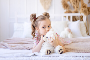 a little child girl at home in a calm natural interior in beige color plays and cuddles with a soft...