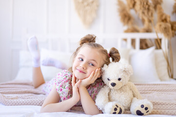 a little child girl at home in a calm natural interior in beige color plays and cuddles with a soft...