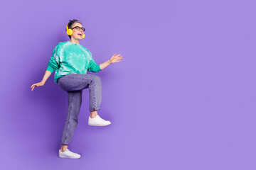 Full body photo of attractive senior woman headphones dance step dressed stylish green clothes isolated on purple color background