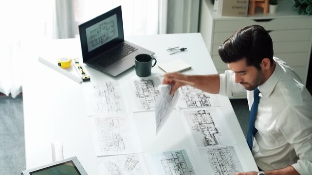 Architect engineer using laptop planning house design at office while sitting at meeting table with blueprint and equipment scatter around.Skilled civil engineer working at blueprint. Alimentation.