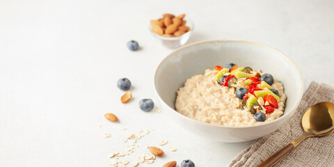 Oatmeal porridge with fruit and berries in bowl on the table. Homemade healthy breakfast cereal with strawberry, kiwi fruits, blueberry and almond