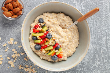 Oatmeal porridge with fruit and berries in bowl on the table. Homemade healthy breakfast cereal with strawberry, kiwi fruits, blueberry and almond. Top view