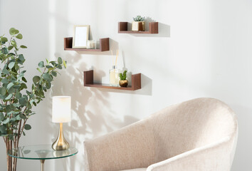 Cozy minimalist living space with floating wooden shelves, a stylish glass side table, framed photos, lush green plants, and a beige armchair, creating a serene and inviting atmosphere for relaxation.