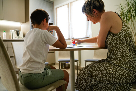 Mother and son smiling while playing Parcheesi in the kitchen.