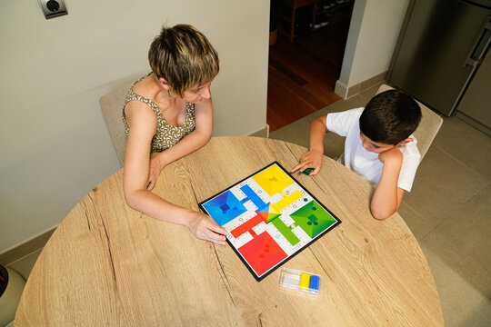 Mother and son playing Parcheesi at home, both deeply engaged in the game.