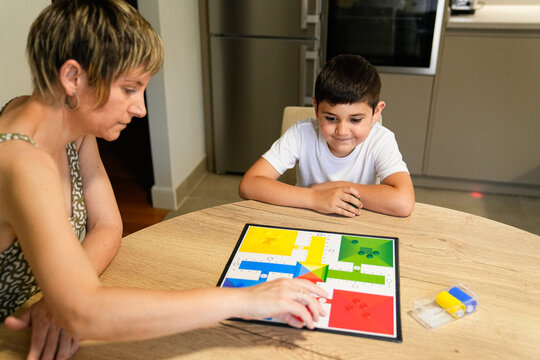 Mother and son deeply engaged in a game of Parcheesi, planning their next moves.