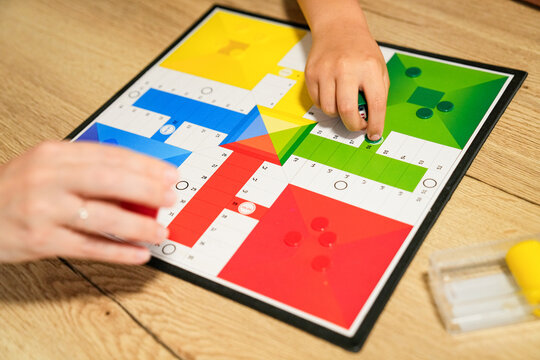Close-up of mother and son moving pieces on a Parcheesi board, focused on the game.