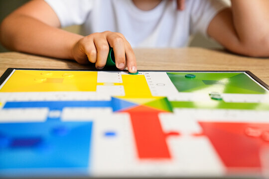 Child moving a piece on a Parcheesi board, focused on the game.