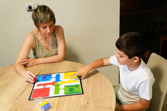 Mother and son strategizing their next moves in a Parcheesi game at home.