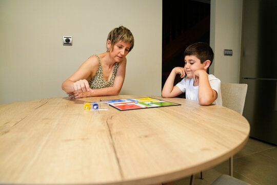 Mother and son focused on a Parcheesi game at the dining table.
