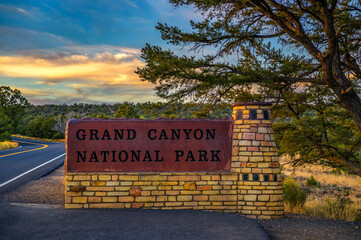 Welcome sign at the entrance to Grand Canyon National Park with a scenic road and trees at sunset.
