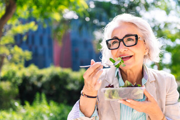 portrait of a middle age woman eating a takeaway salad sitting outdoors in a city park, concept of...