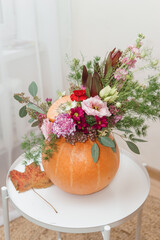Flower arrangement in a pumpkin, autumn interior decor. Creating handmade autumn decor.