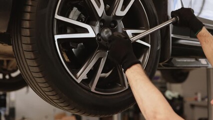 Mechanic performing tire maintenance using tools in auto repair shop. Close-up of gloved hands operating on car wheel, ensuring proper functionality and safety.