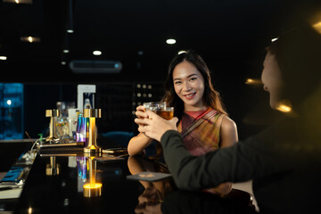 Attractive asian woman clinking glasses of whiskey with her friend at bar counter. Nightlife and friendship concept