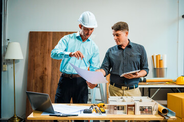A Caucasian male engineer and an Italian male building contractor are planning and talking at a...