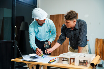A Caucasian male engineer and an Italian male building contractor are planning and talking at a...
