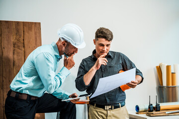 A Caucasian male engineer and an Italian male building contractor are planning and talking at a...