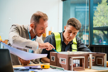 A Caucasian male engineer and an Italian male building contractor are planning and talking at a...