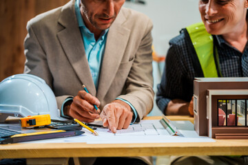 A Caucasian male engineer and an Italian male building contractor are planning and talking at a...