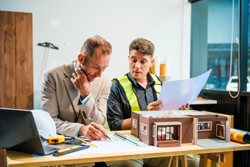 A Caucasian male engineer and an Italian male building contractor are planning and talking at a...