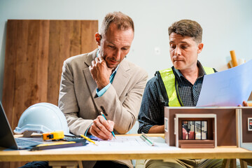 A Caucasian male engineer and an Italian male building contractor are planning and talking at a...