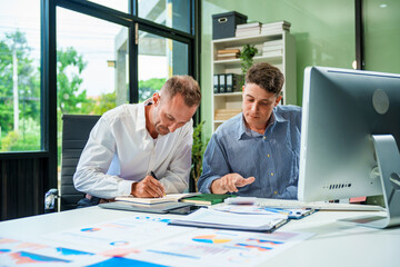 An Italian male and a Caucasian male sit at business desk in office meeting room, discussing...