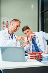 Obraz premium In a hospital meeting room,Italian male and Caucasian male discuss medical cases at desk with X-ray films, blood samples, patient information, on diagnosing heart disease and treatment guidelines.