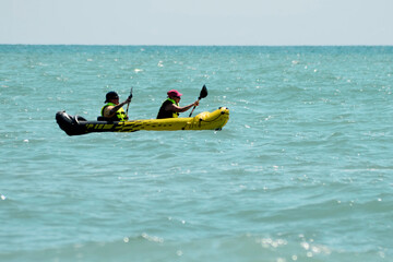 Two people in life jackets on a kayak paddling in the open ocean with calm water. Water sports, olympic games, lifestyle