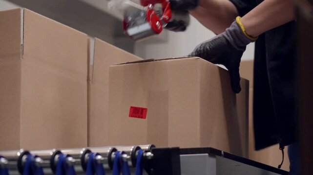 Worker assembling the box from the cardboard, close shot of a labour folding the board into a carton and sticking the tape to seal it. Production belt process in a factory.