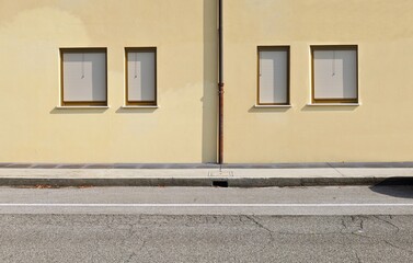 Rusty roof gutter on yellow plaster wall with row of closed windows by venetian blinds. Concrete...