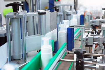 Production of cosmetics and skin care products. A white plastic bottle is moving along a conveyor belt. A capping and labeling machine.