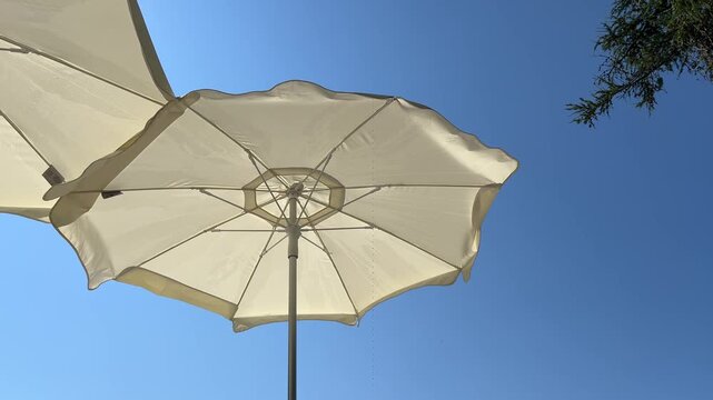 White sun umbrellas on the beach. Vacation time in summer. Two beach umbrellas with blue sky in the background. Relaxing on the sea shore on a sunny day.