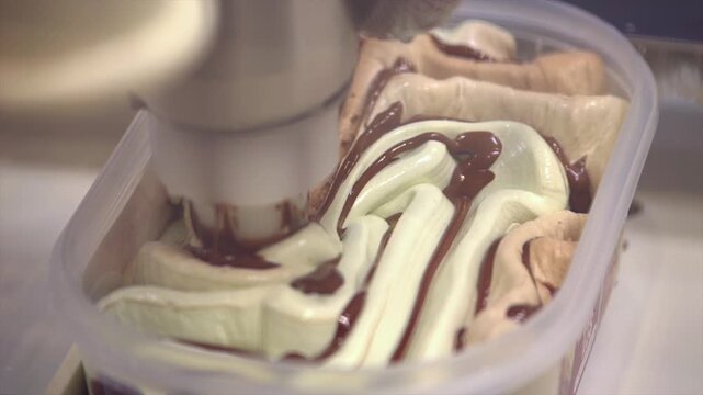 Close shot of a mechanical arm filling the freshly made ice-cream in a pattern in squround container. Hygienic, slow motion production belt process in ice cream factory.