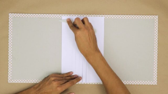 Hands crafting a hand-bound book with precise folding and attention to detail, top view