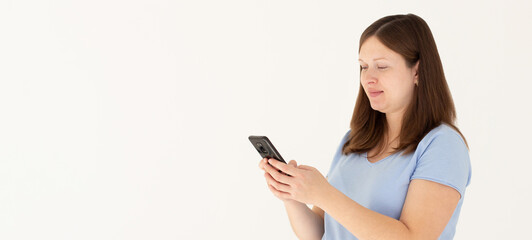 Fototapeta premium Happy pretty young woman model holding smartphone looking at cell texting message, smiling girl using mobile apps on cell phone standing isolated on white background with cellphone.