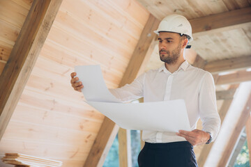 Architect wooden buildings. Man stands under frame wooden house. Man architect studies...