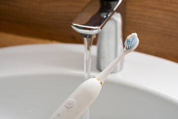 Upright electric toothbrush on sink edge, faucet background.