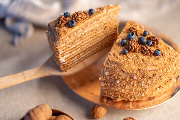 One slices of layered honey cake topped with blueberries and nuts, placed on a wooden spatula and plate