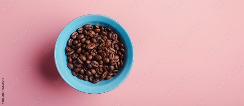 Poster view from above of a blue cup filled with coffee beans on a pink background surrounded by copy space