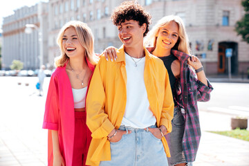 Group of young three stylish friends posing in the street. Fashion man and two cute female dressed in casual summer clothes. Smiling models having fun. Cheerful women and guy outdoors
